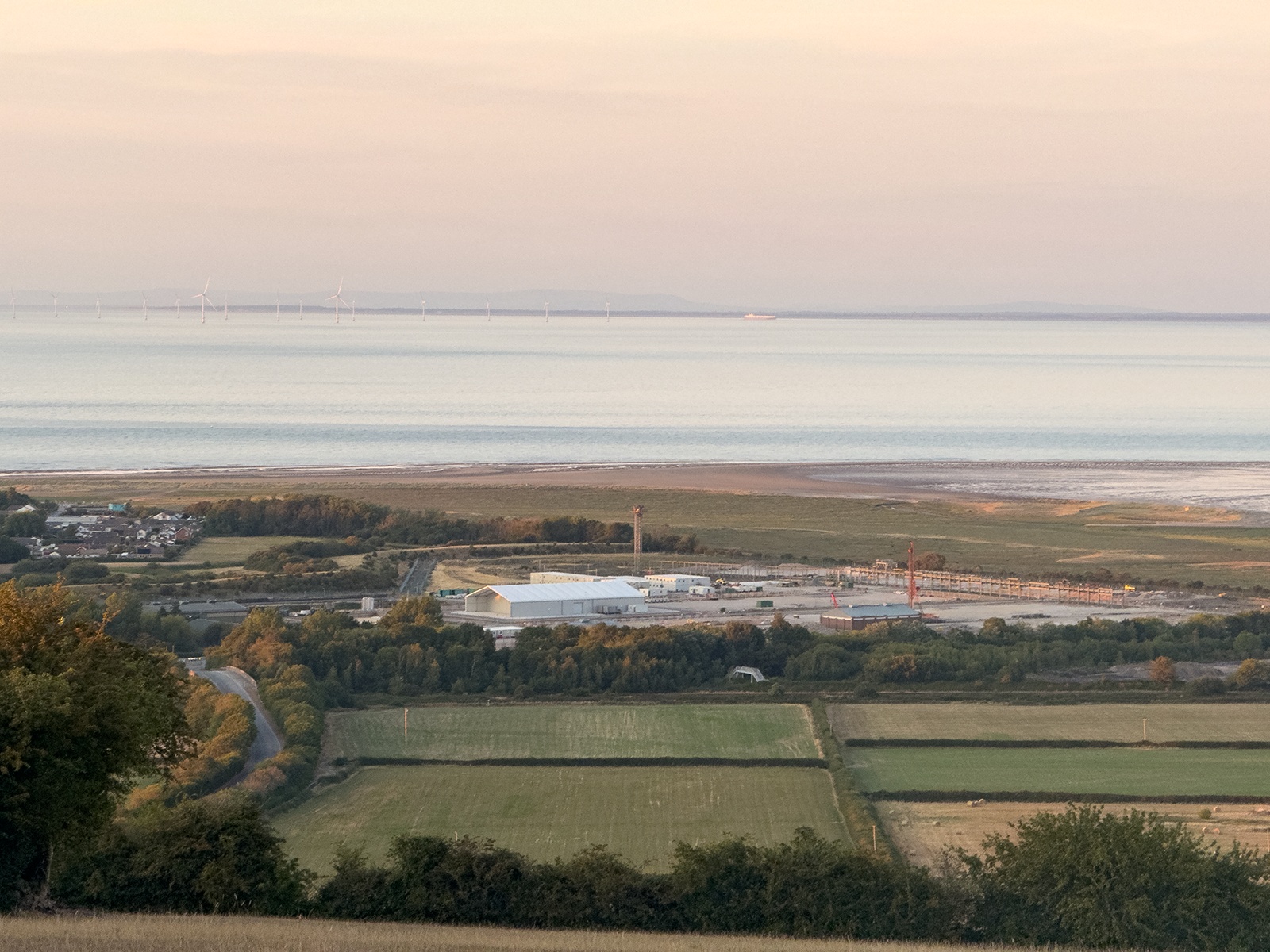 Landscape view over Point of Ayr, North Wales, looking across fields and the estuary toward wind turbines on the horizon at dusk.
