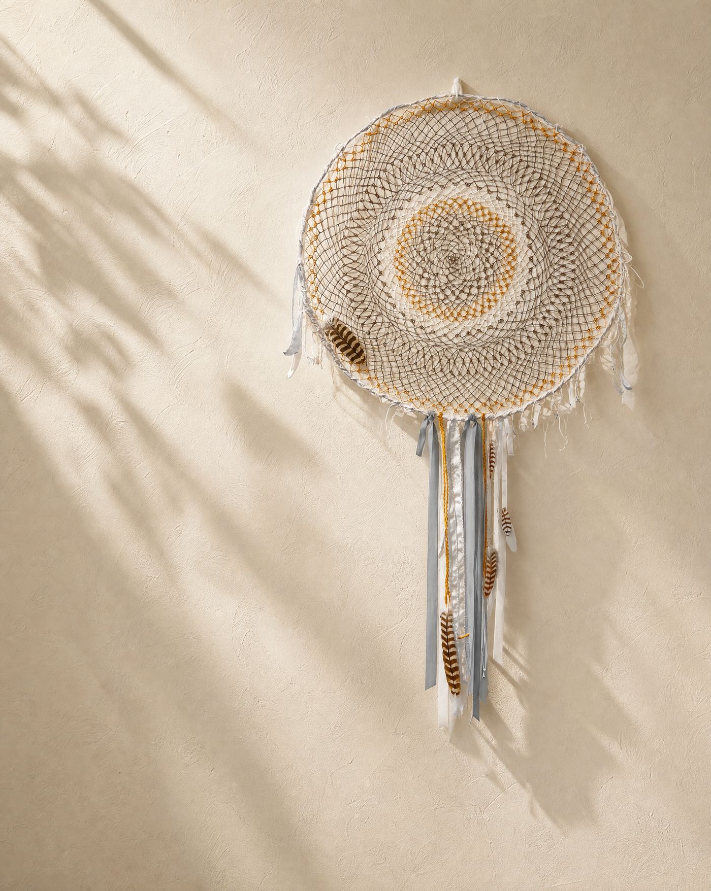 Silent Flight, an 86cm handcrafted dreamcatcher with a concentric cream and ochre weave and Gyr/Saker falcon feathers.